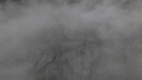 heavy fog with rocky mountain side in background, aerial side flying shot