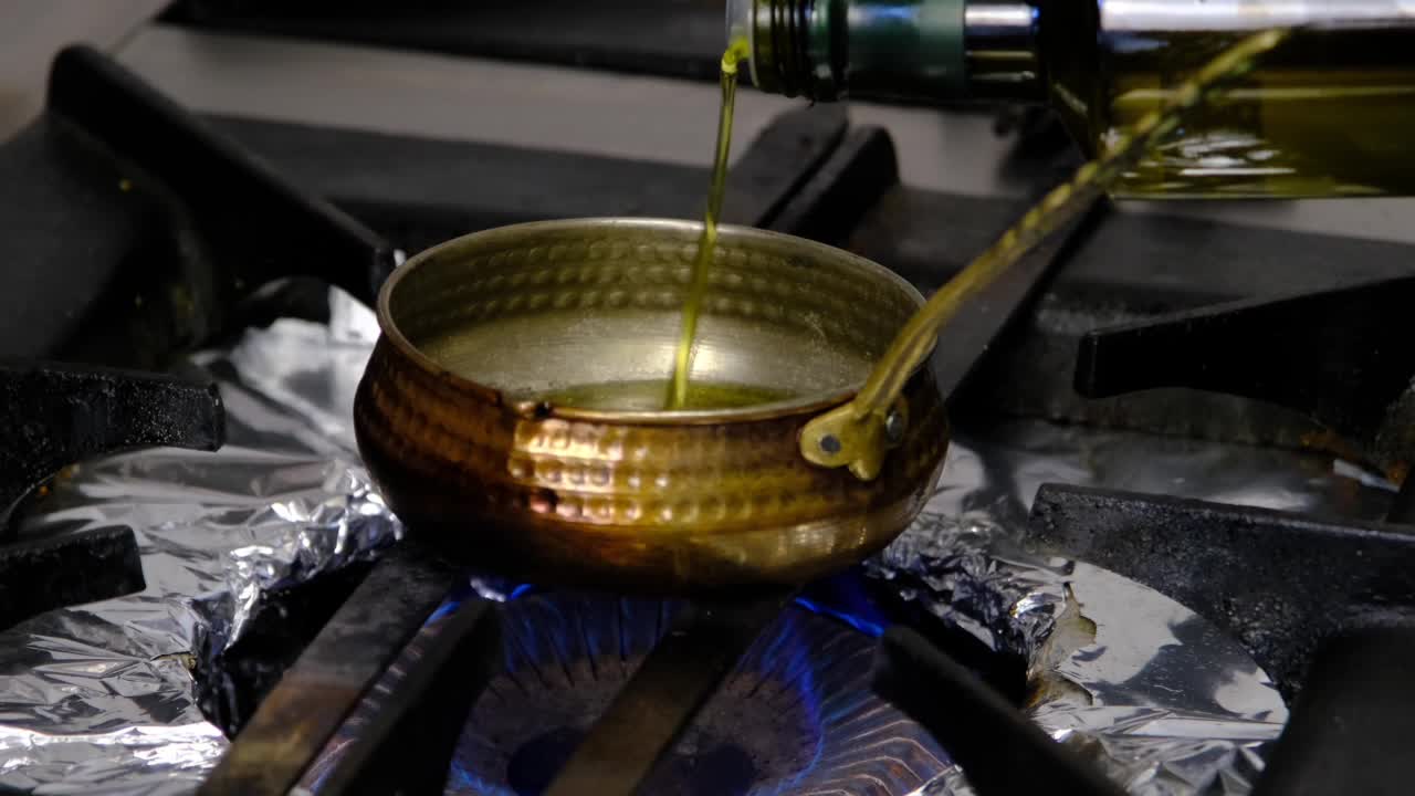 повар наливает масло в пустой горшок на плите