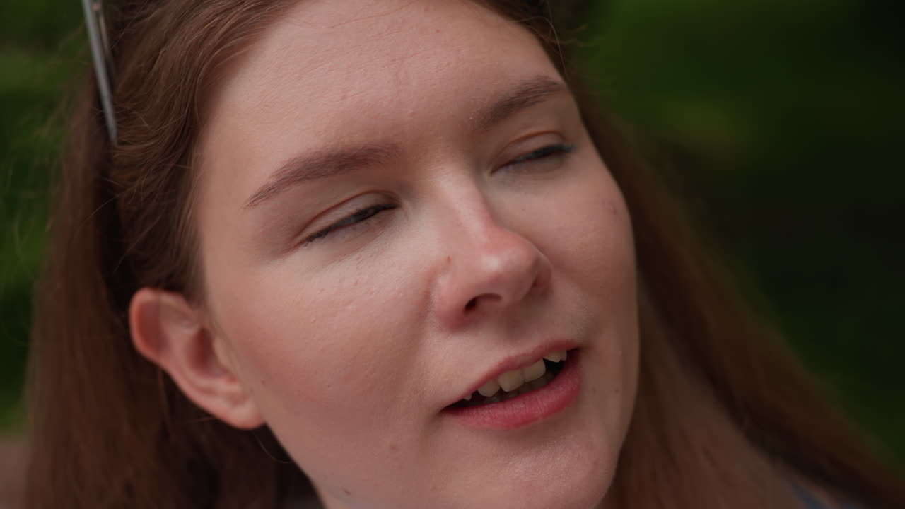 Close up of young woman in casual outfit sitting on wooden park bench sipping water from clear plastic bottle with satisfied expression, enjoying refreshment