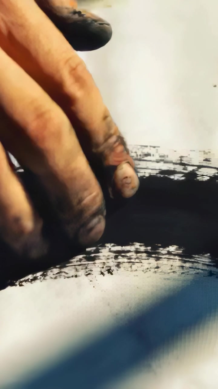 Vertical video: Smearing hand touching black ink, pressing to blend on paper under blue shadow