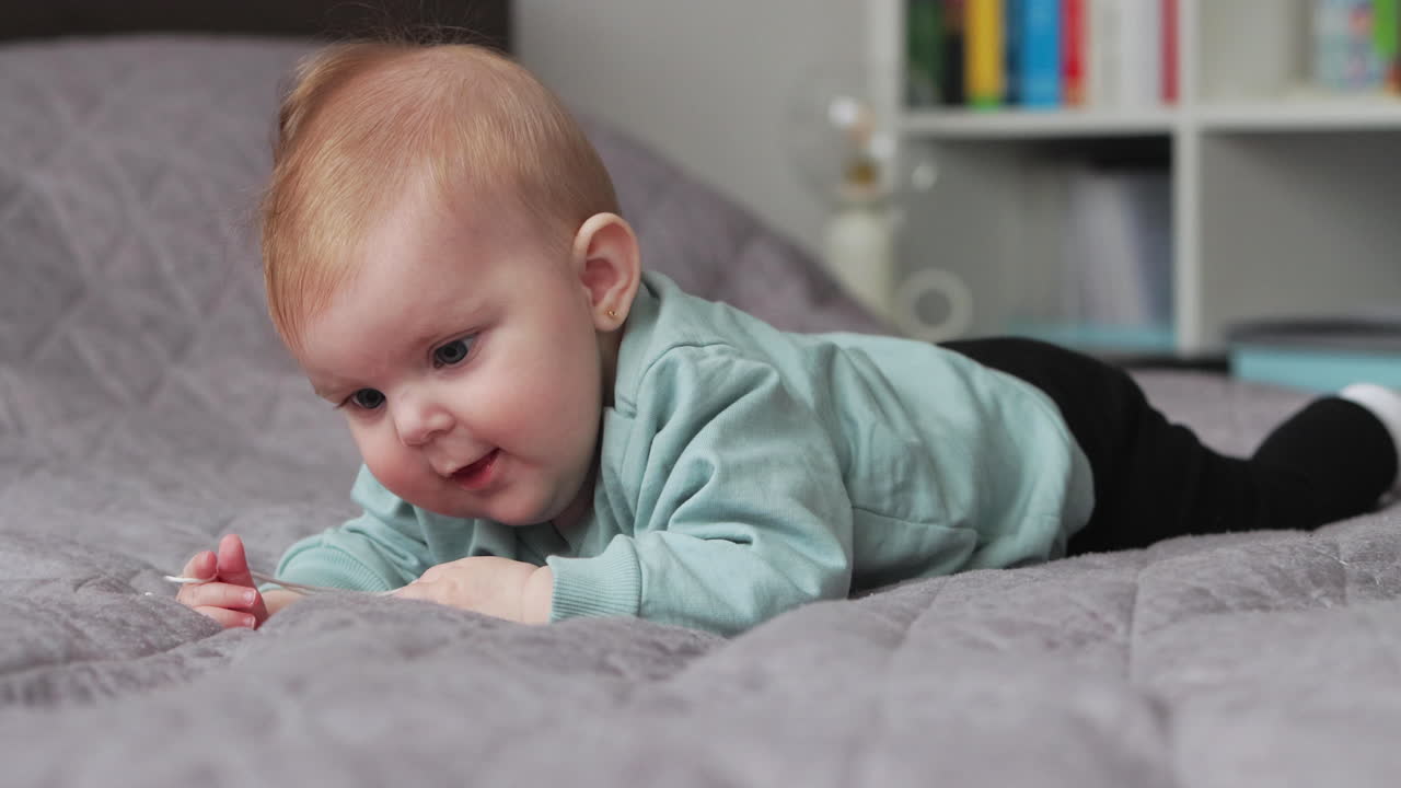 una niña sonriente y feliz sobre una manta acostada boca abajo juega con un juguete para masticar