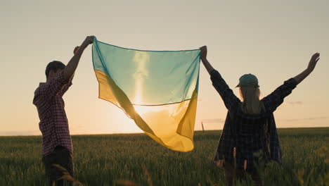 energetic ukrainian couple raising the flag of ukraine over a field of wheat at sunset