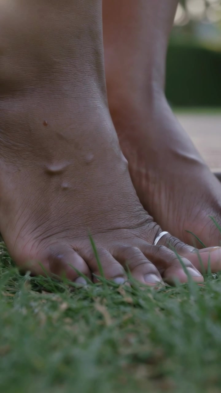 Video verticale: Piedi di adulto che toccano l'erba, premendo e posandosi sul prato, con anello d'argento all'alluce