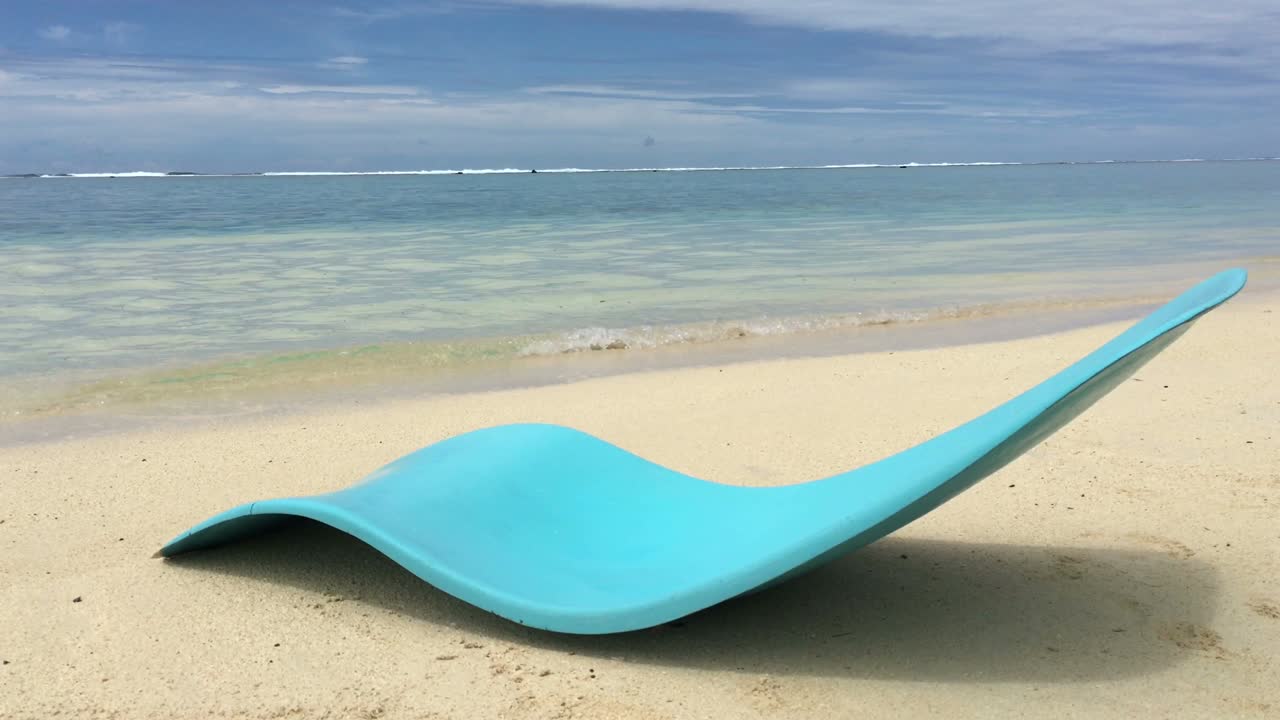una silla de playa azul vacía en una playa de arena de una isla tropical del pacífico
