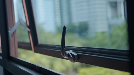 close-up of an open window with a handle, providing a view of blurry trees and buildings outside