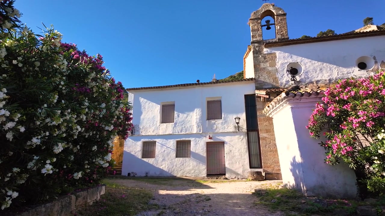 Vista di una chiesa tradizionale imbiancata a calce e di edifici storici vicino al Castello di Xativa a Valencia, Spagna, circondati da arbusti fioriti in una giornata di sole.