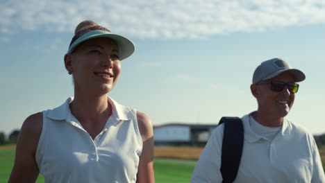 two golf players walk country club course. smiling couple talking sport outside.