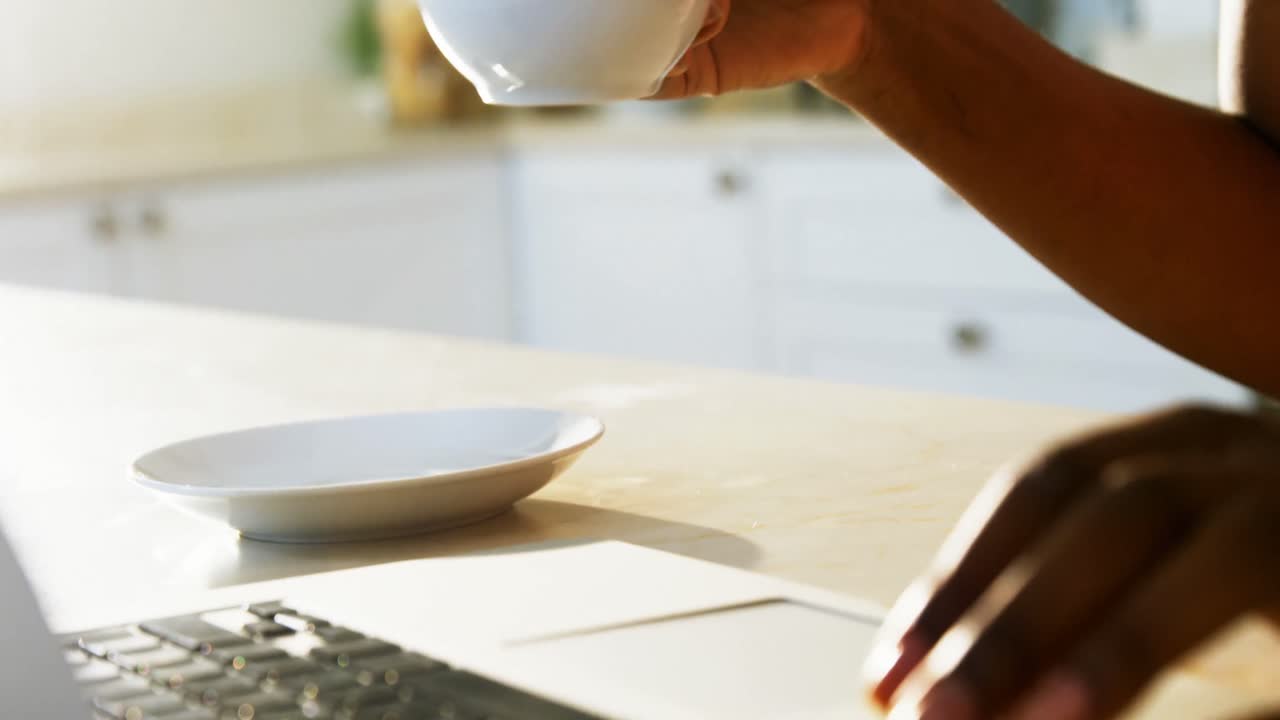 mujer usando una computadora portátil mientras toma café en la cocina