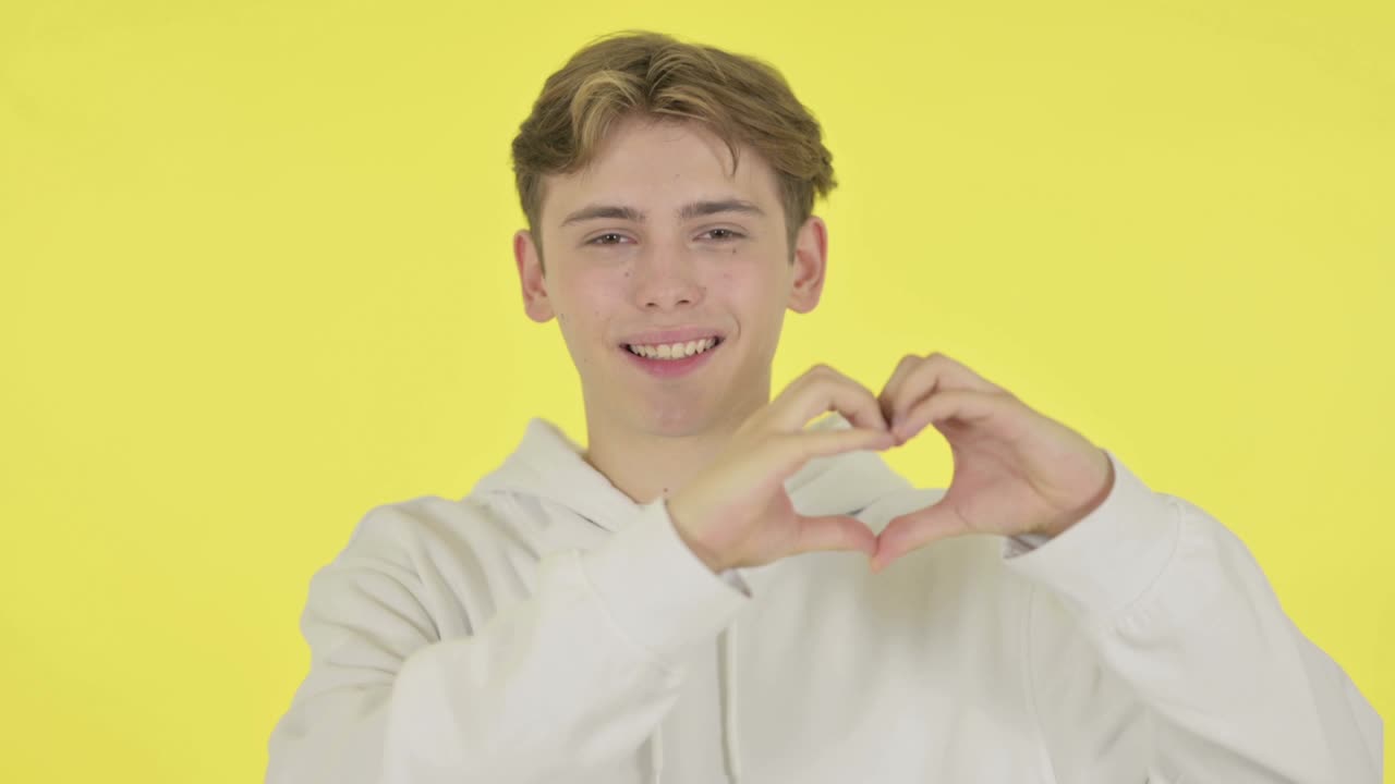 노란색 배경 에 손 으로 심장 모양 을 보여 주는 젊은 남자