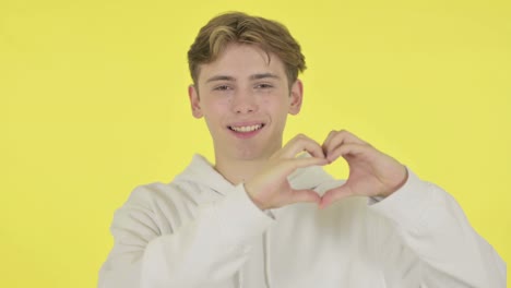 young man showing heart shape by hands on yellow background