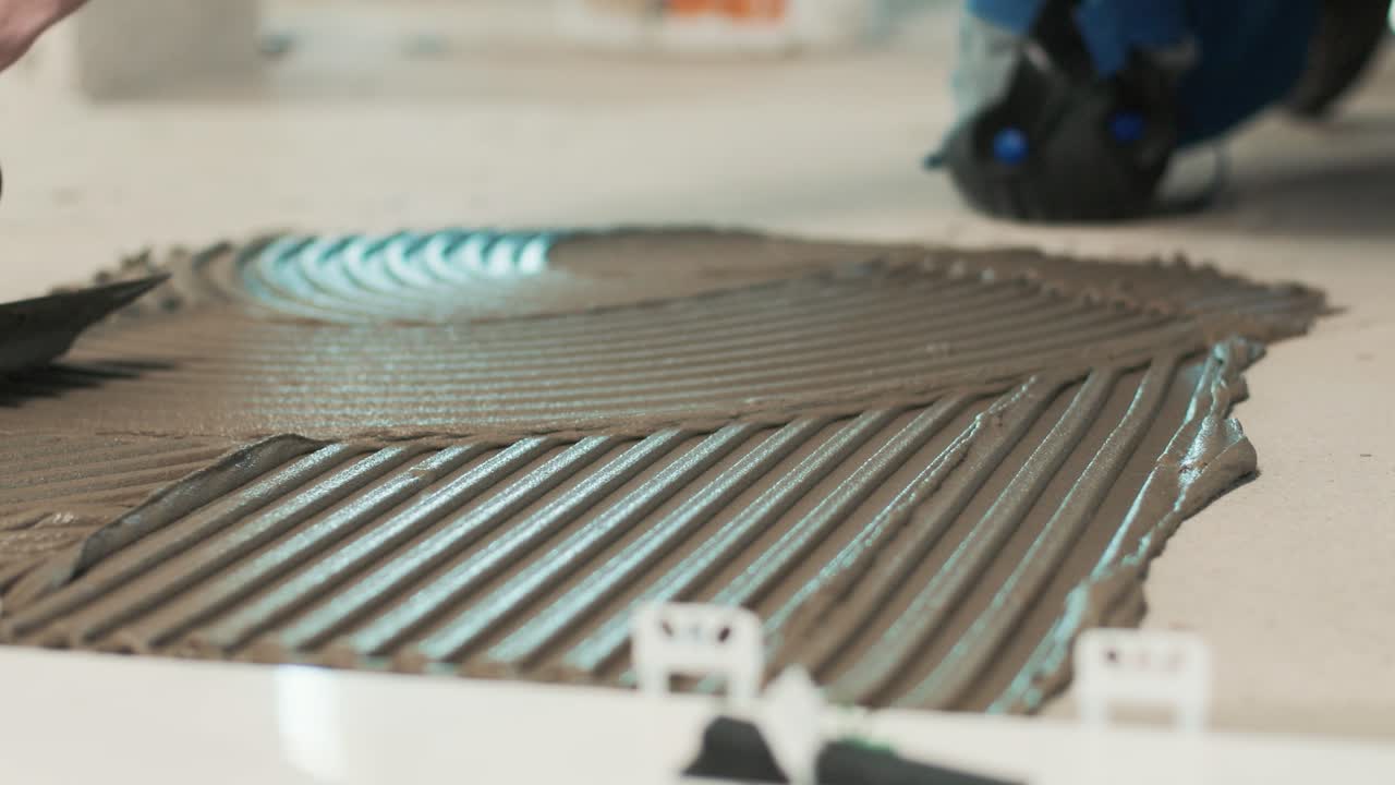 Person spreading tile adhesive on the floor with a notched trowel