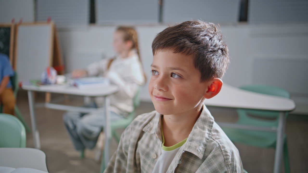 Portrait small kid sitting lesson in classroom. Smiling schoolboy looking camera