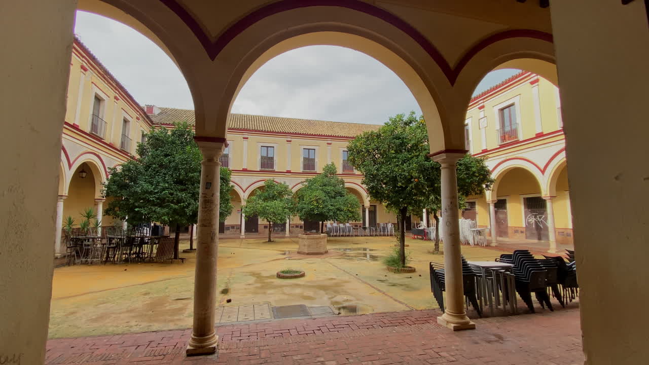 Tranquillo cortile appartato con archi, aranci e sedie vuote, luce soffusa dopo la tempesta in un antico edificio andaluso