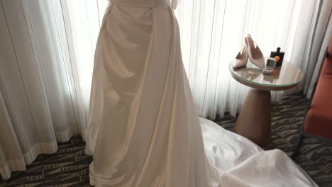 white wedding dress with long train on mannequin in hotel room during wedding day