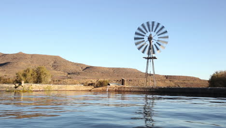 agricultural water pump turns in a farm setting pumping water into a storage tank against an arid landscape in south africa