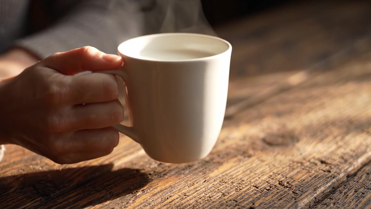 Un momento accogliente di relax catturato in due fotogrammi, con una mano che tiene delicatamente una tazza fumante di bevanda, evidenziando i piaceri semplici e la tranquillità di un'atmosfera serena.