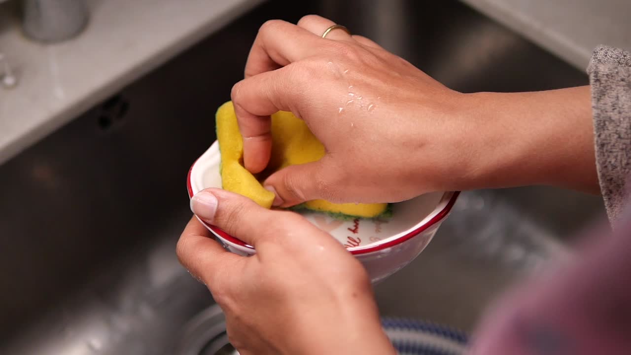 Primer plano de manos lavando un tazón pequeño con una esponja en un fregadero de cocina