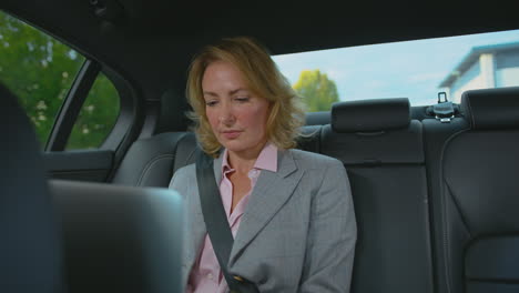 mature businesswoman sitting in back seat of taxi or car working on laptop