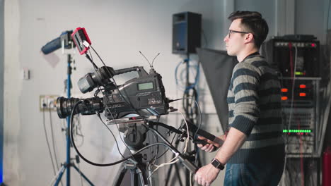 man operating professional video camera in studio setting. adjusting camera equipment on tripod during filming. technician using camera rig with additional accessories in production studio