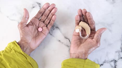 hands holding a pill and hearing aid