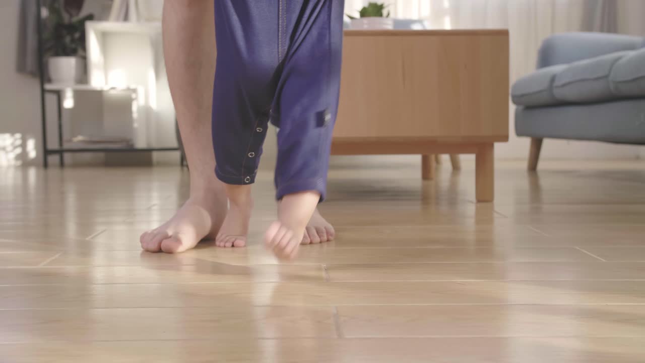 Baby Boy Learning To Walk And Make His First Steps. Father Is Holding His Hand. Child'S Feet Close Up