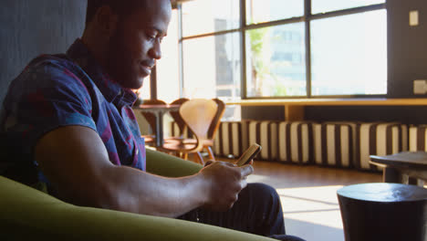 Side-view-of-young-black-businessman-texting-and-talking-on-mobile-phone-in-a-modern-office-4k