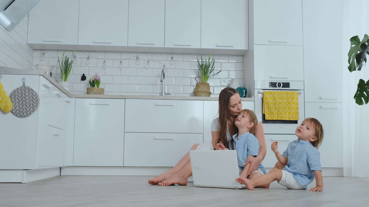 현대적인 기술. 현대적인 아파트 사랑하는 엄마와 두 작은 아들이 거실 바닥에 앉아 노트북 화면을 보고 있습니다. 엄마와 함께 아이들은 노트북에서 놀고 있습니다.