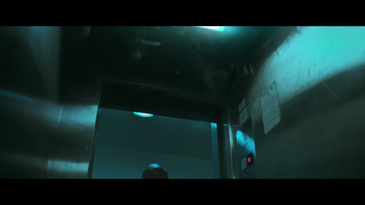 A bald dangerous looking man prepares a gun with the silencer in the elevator