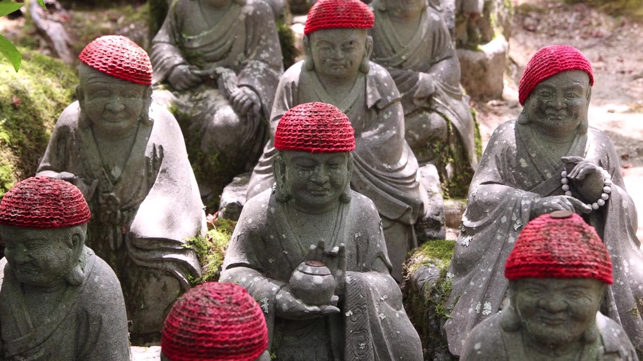 Rader av Jizo-statyer i sten, bärande röda mössor och haklappar, under traditionella firanden av Kangen Sai-festivalen på Miyajima-ön, Hiroshima, Japan