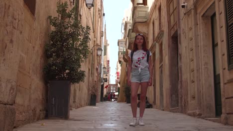 young woman standing in the street while looking at historic buildingin valletta, malta