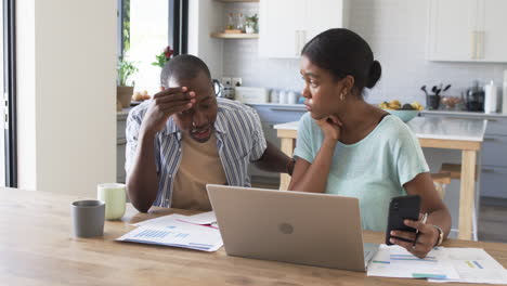 a young african american couple is managing finances at home using a laptop