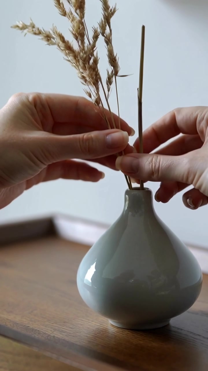 Vidéo verticale: Plaçant une tige, mains arrangeant des brindilles dans un vase en céramique sur une table en bois, équilibrant des roseaux