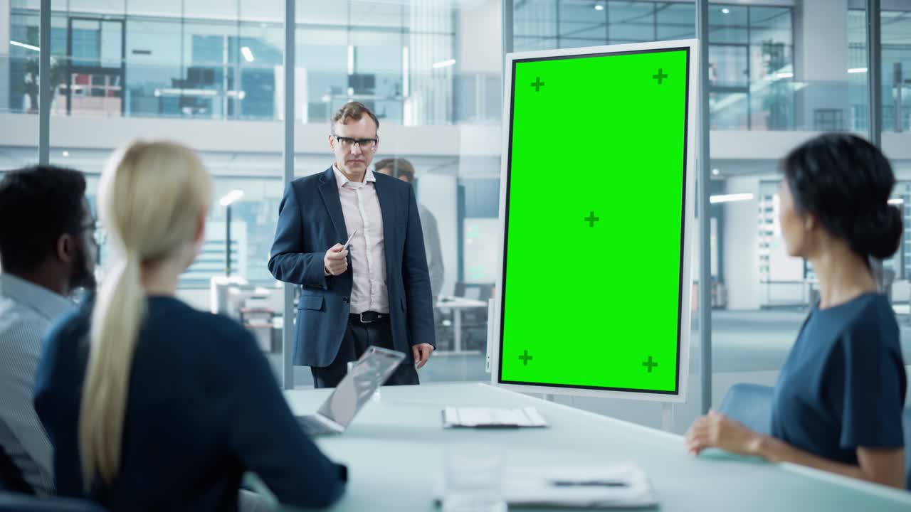 회사 운영 관리자는 경제학자 팀을 위해 회의 프레젠테이션을합니다. 성인 남성은 수직 녹색 화면 모의 디스플레이와 함께 디지털 화이트보드를 사용합니다. 사람들은 비즈니스 사무실에서 일합니다.