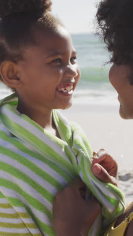 smiling african american mother toweling off her daughter on sunny beach