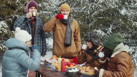 friends toasting with drinks at campsite in winter forest