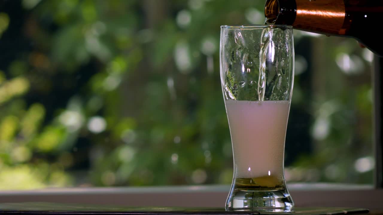 Pouring Beer Into a tulip Glass with plants on the background in slow motion-1