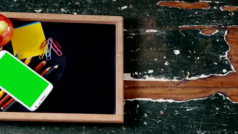 apple and mobile phone with school supplies on slate