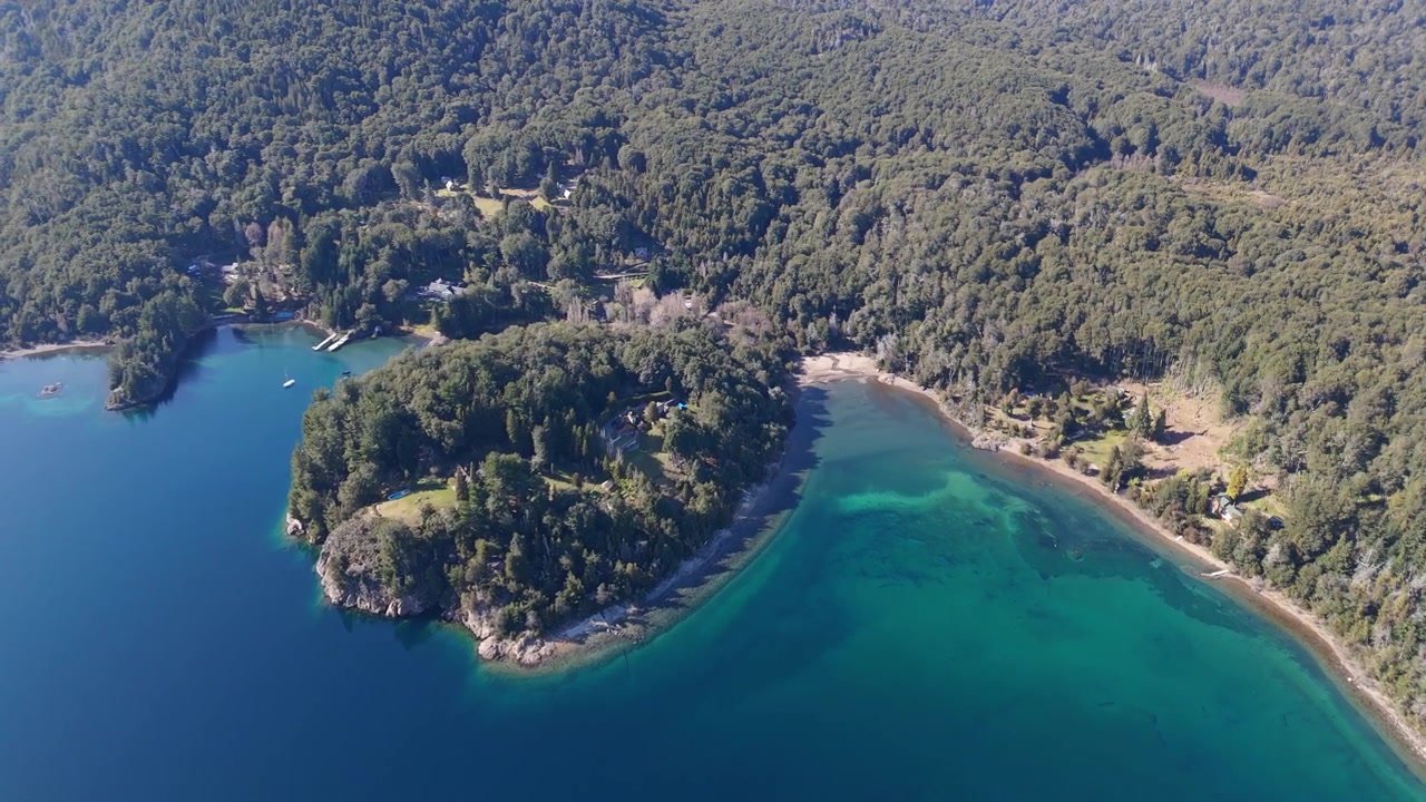 Letecký pohled na břeh jezera Nahuel Huapi se smaragdově zelenou vodou a borovými lesy.