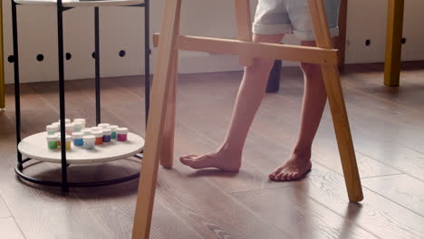 camera focuses on the feet of a girl who is painting on the lectern