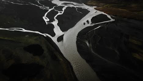 aerial tilt up thor valley, flying over glacial river flowing through black volcanic mountains, thorsmörk dramatic moody landscape iceland