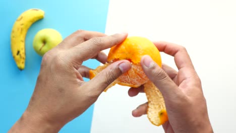 peeling an orange: a close-up view of hands peeling a juicy orange with banana and apple in the background