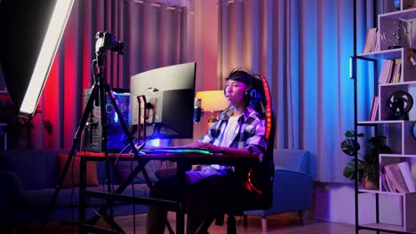 asian boy streamer playing game over network on personal computer. challenge and bully threat killing competitor, live stream video game, desk illuminated by rgb led strip light