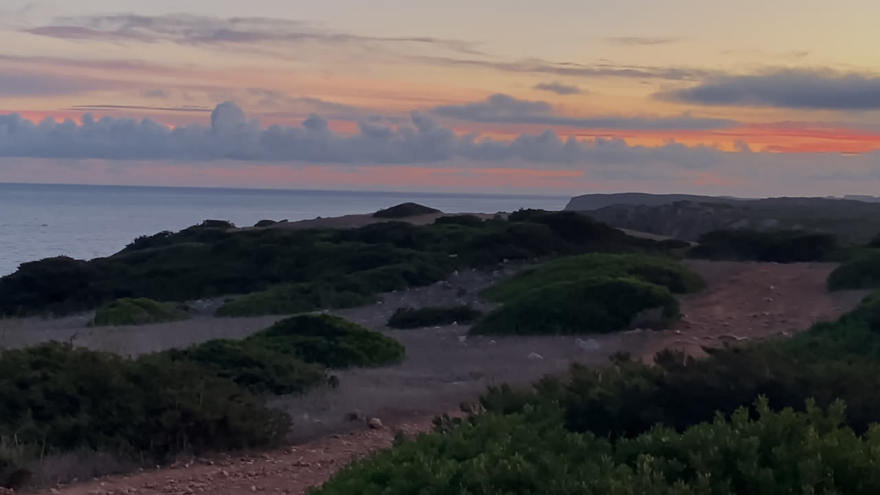 The sky burns in shades of orange and pink above Sagres cliffs as night approaches the Atlantic A crescent moon rises above the calm Atlantic waters of Sagres during twilight
