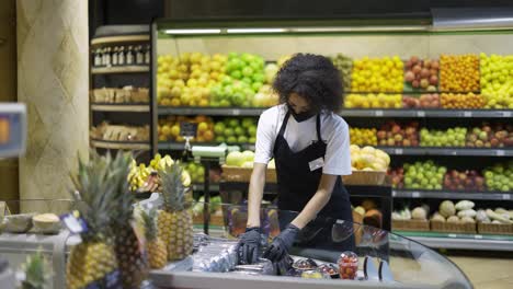 Female-grocery-store-employee-in-face-mask-and-gloves-checking-freshness-of-products-in-store