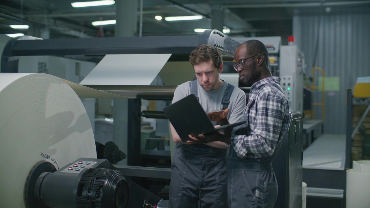 Printing Factory Operators Analyzing Data on Laptop near Large Paper Reel