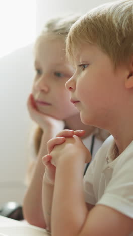 couple of children watches cartoons on laptop together. brother and sister sit at desk with folded hands. calm siblings rest together at home closeup