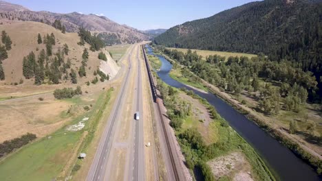 Toma-Aérea-Del-Tren-Conduciendo-A-Lo-Largo-Del-Río-Y-La-Carretera