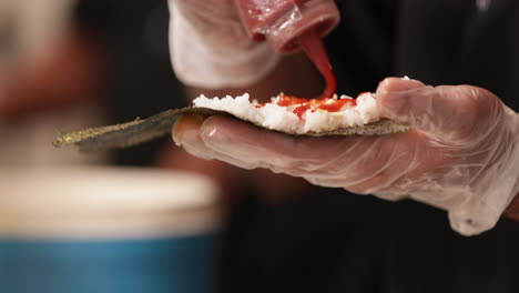 agregar salsa picante al arroz de sushi en una envoltura de algas - cerrar