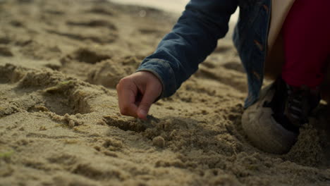 happy child playing sand on ocean beach. smiling kid having fun alone at shore.