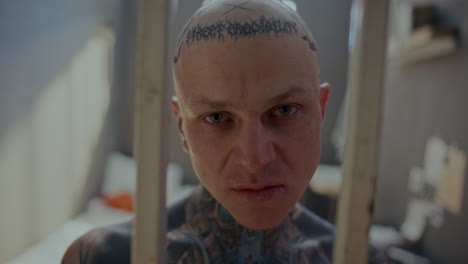 portrait of tattooed inmate with evil look staring through prison cell bars